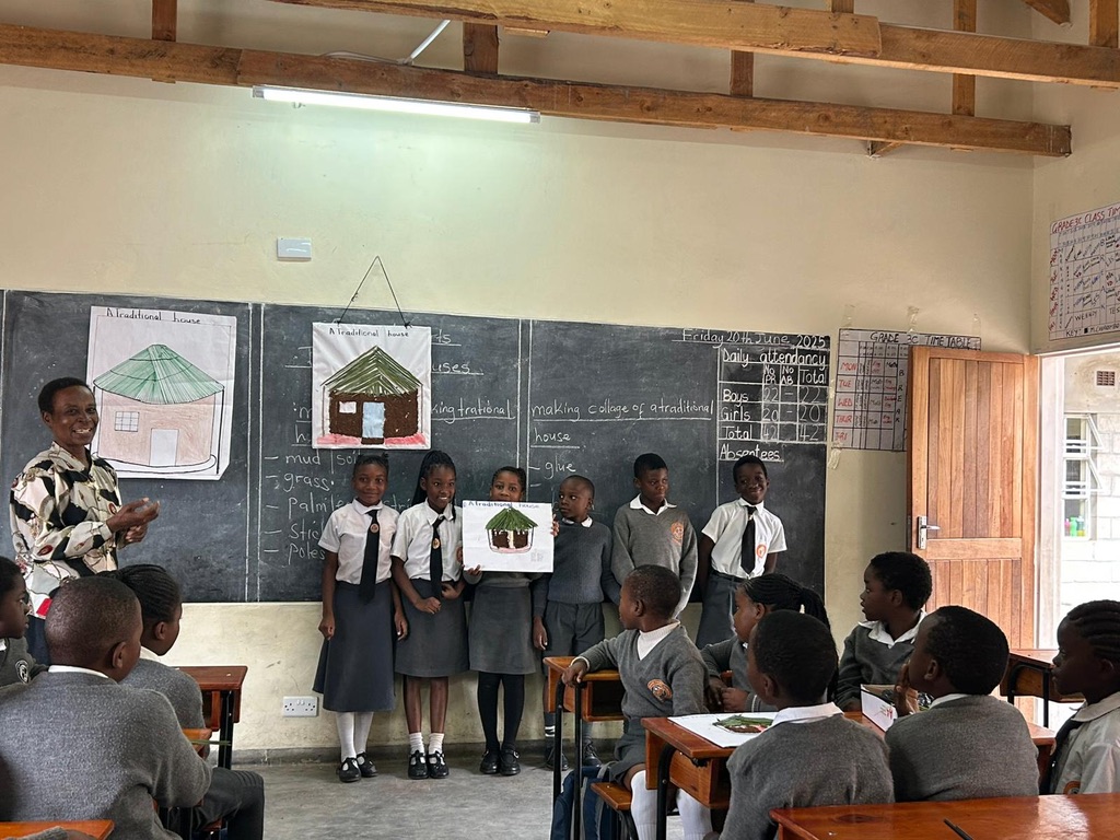 A group of children holding up their work to show the class during a visit from The Blue Coat School Birmingham to establish The Blue Coat Malawi Project