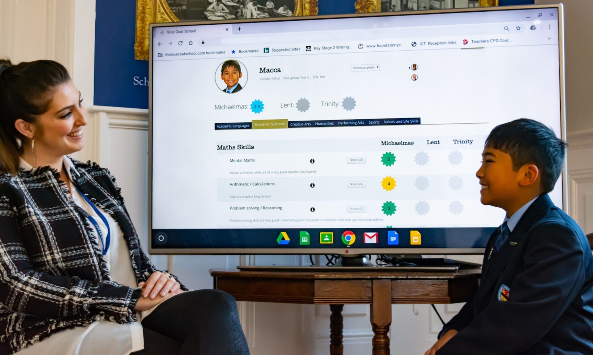 A teacher and a pupil sit in front of a screen showing the pupil's BCS Blue targets and grades.