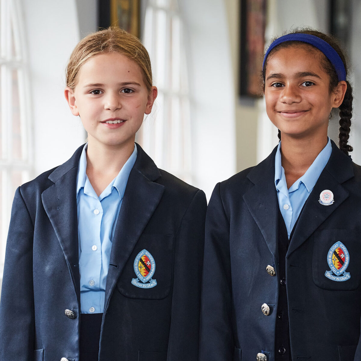 Two girls walking down the corridor and smiling at the camera.