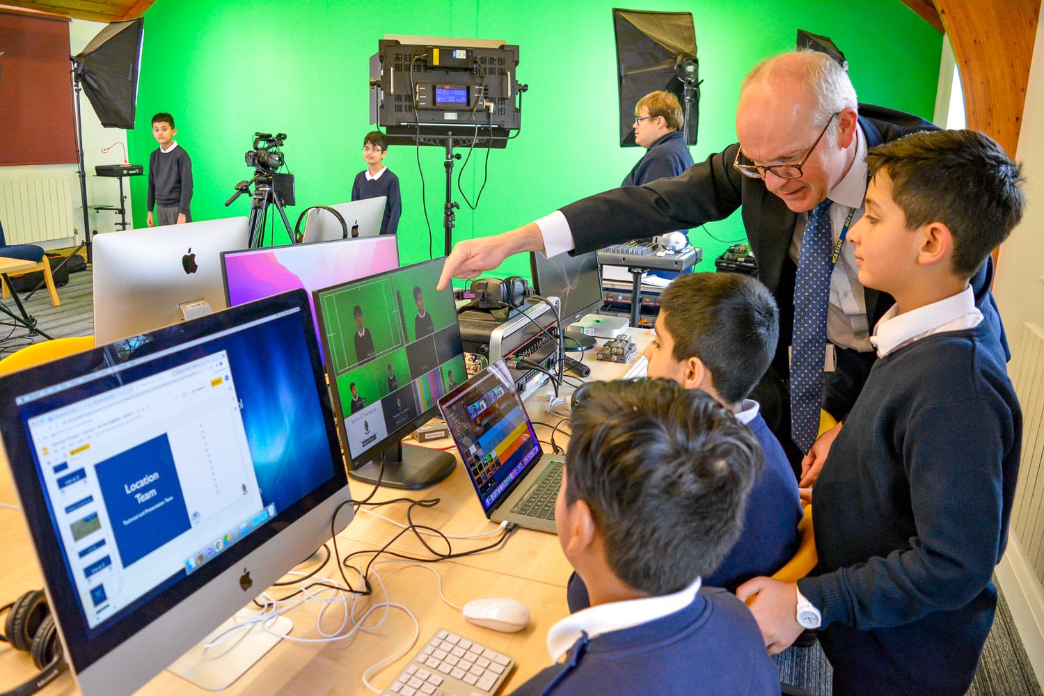 A teacher shows a group of pupils how to use video editing software on Apple iMacs during an enrichment day with a partner school.