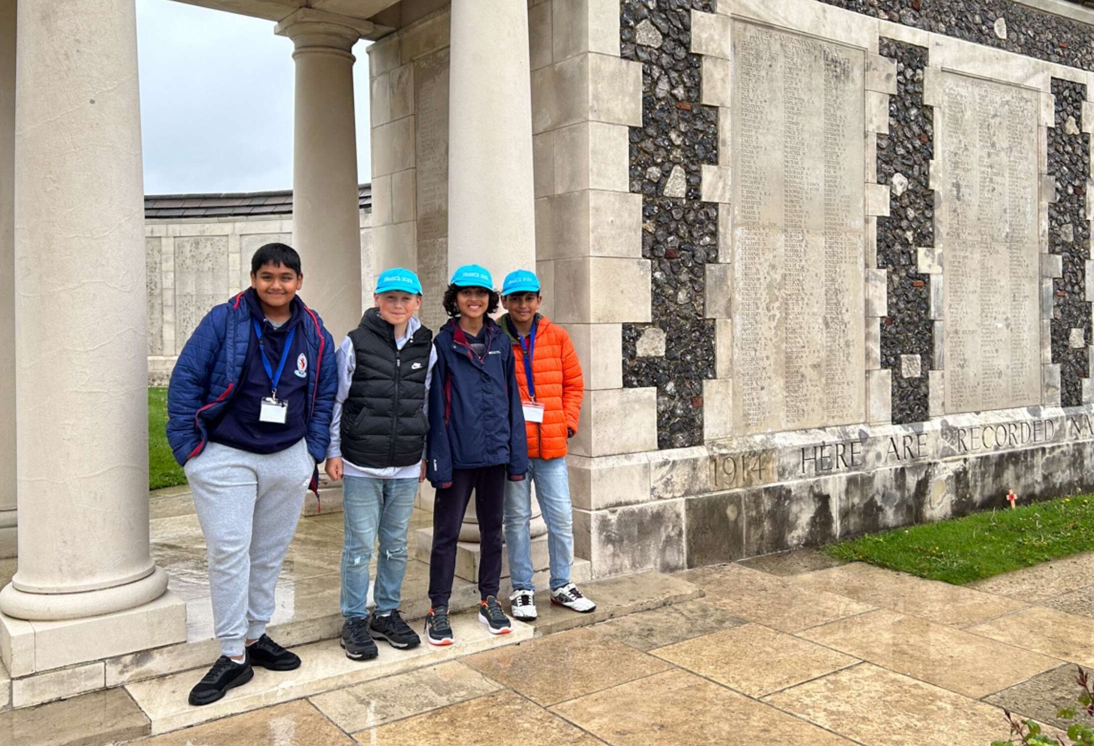 Four pupils stand outside of a war memorial in France.