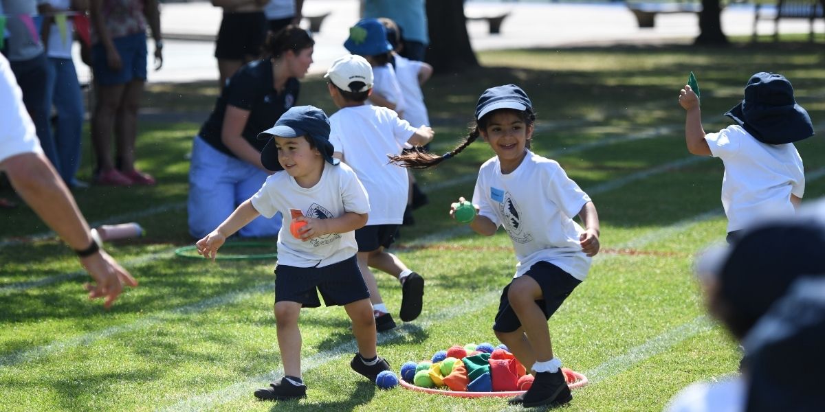 Two Pre-Prep pupils have picked up a bean bag and are running back to their team in a Pre-Prep Sports Day game.