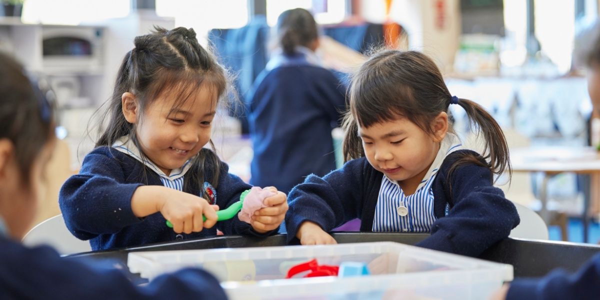 Two girls are smiling whilst playing in the sand in a Pre-Prep classroom at The Blue Coat School