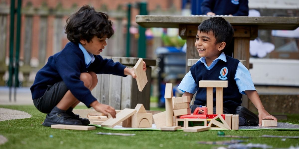 Two boys are sat in the playground building a tower with wooden blocks.