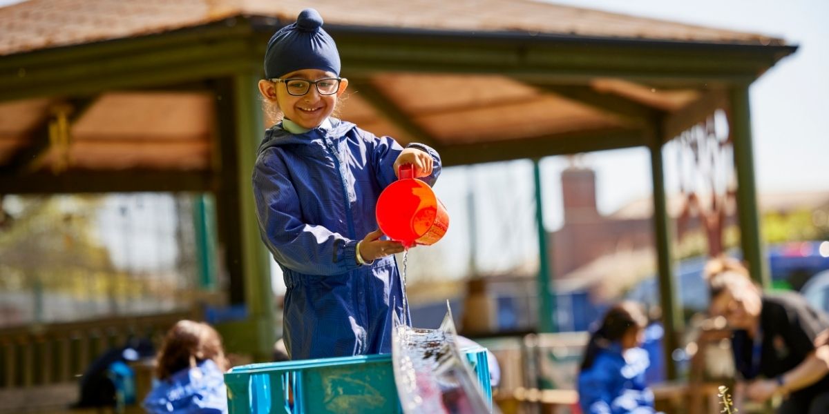 A boy pours water from a jug down a funnel in Forest School at The Blue Coat School Birmingham.